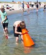 En flok skolebørn i strandkanten. En af drengene undersøger havbunden gennem en orange vandkikkert.
